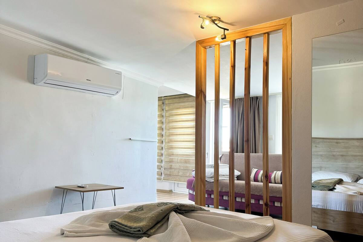 A hotel room with a bed, a small table, a sofa, a wooden partition, and a mirror.