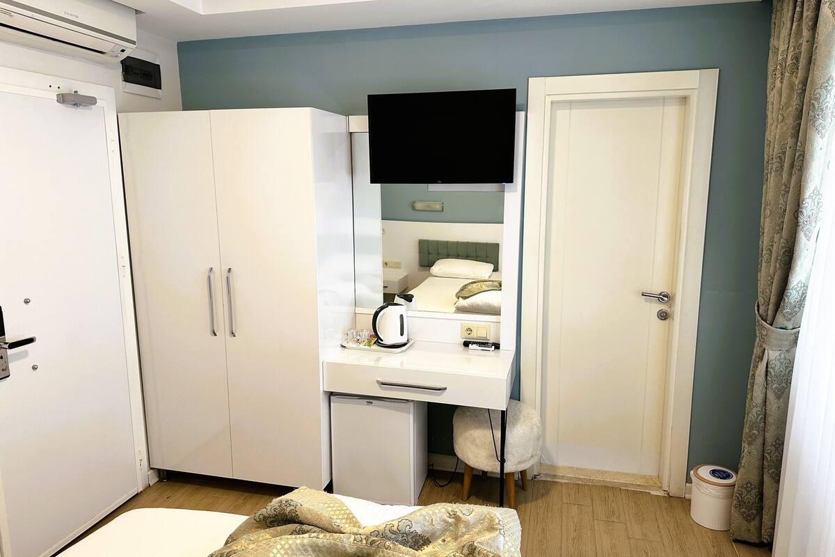 A hotel room with a bed, a desk with a chair, a wardrobe, a television, and a door.
