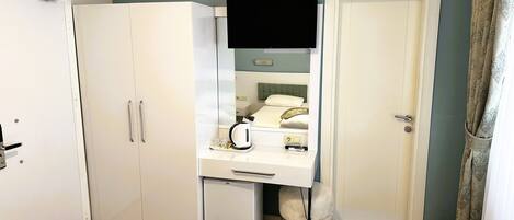Habitación de hotel con cama, escritorio, silla, armario, televisor y puerta.