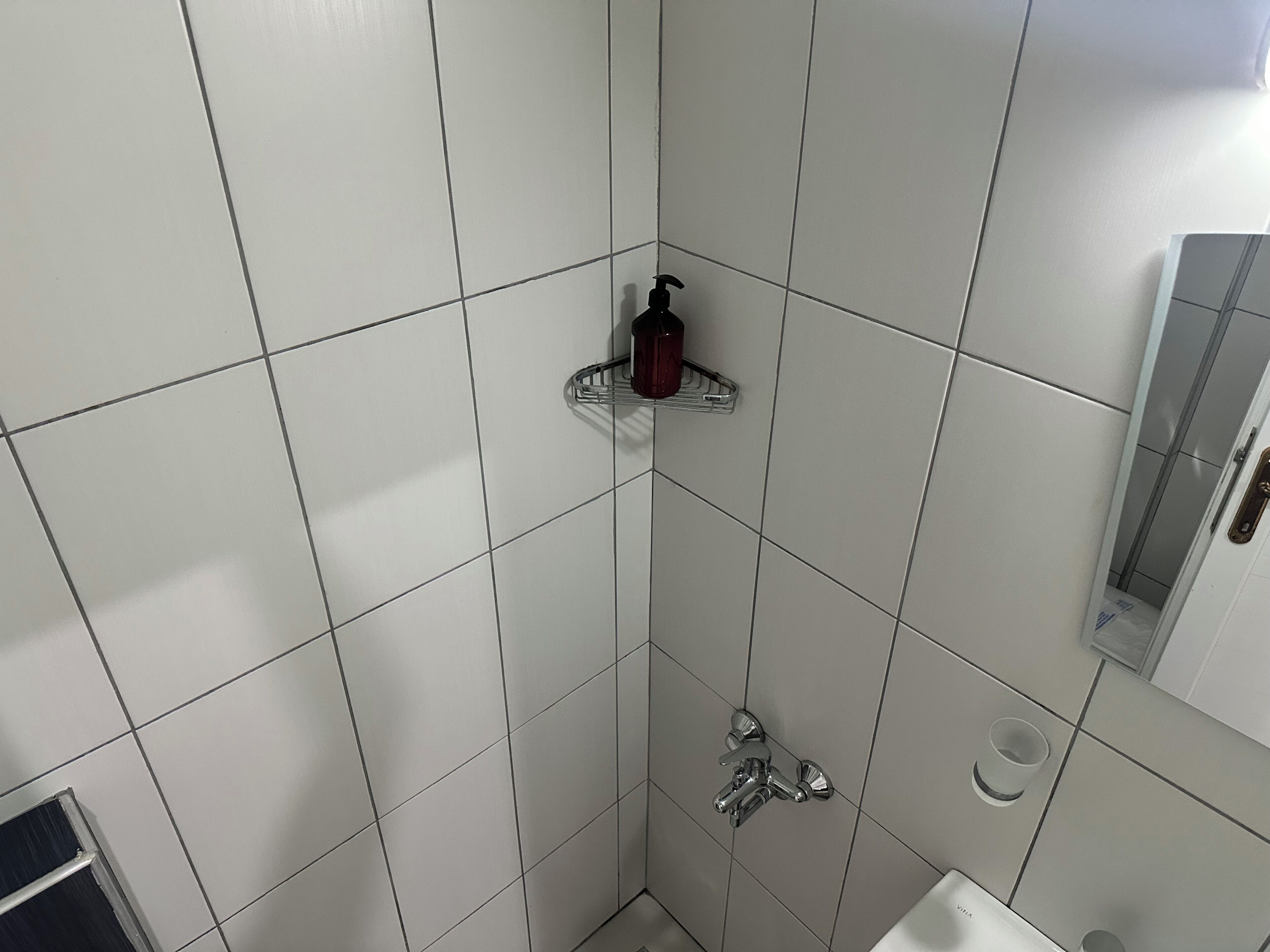 Ein Badezimmer mit weißen Fliesen, einer Dusche, einem Händetrockner und einem Spiegel.