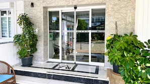 A hotel entrance with a glass door, a staircase leading up, and potted plants on either side. - Amsterdam Otel & Suites  (Kemer)