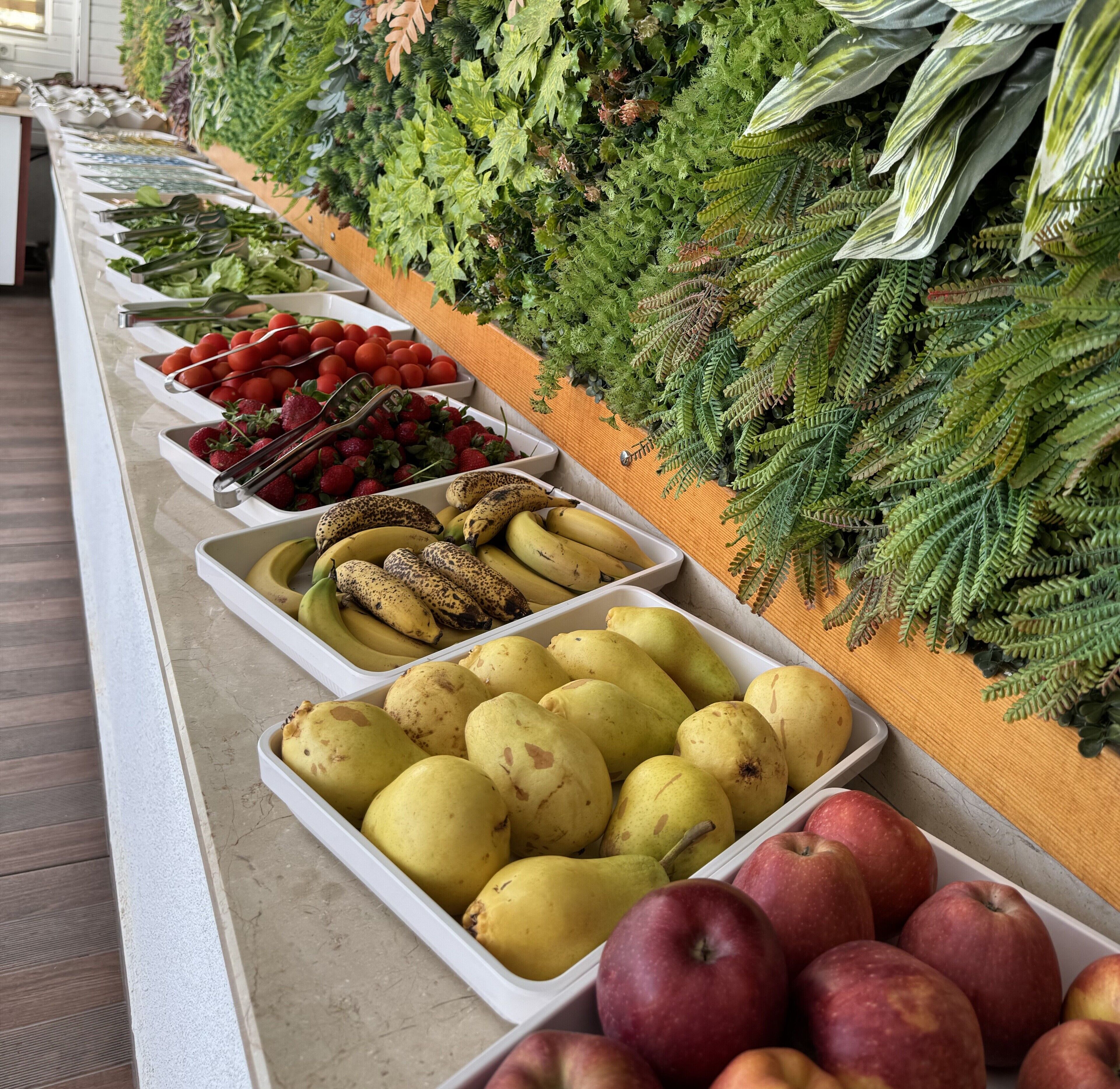 En buffet med et udvalg af frugt og grøntsager, herunder jordbær, bananer, pærer og æbler.