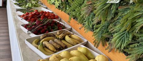 En buffet med et udvalg af frugt og grøntsager, herunder jordbær, bananer, pærer og æbler.