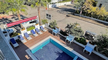 A rooftop pool area with lounge chairs, a sign indicating a location, and surrounding greenery.