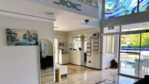 A hotel lobby with a reception desk, framed certificates, a large mirror, and a view of the outdoor area. - Amsterdam Otel & Suites  (Kemer)