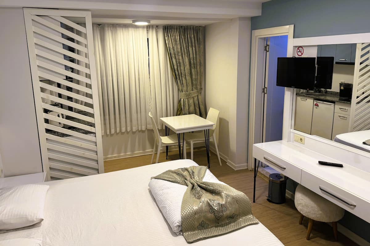 A hotel room with a bed, a desk with a computer, a chair, a TV, and a wardrobe.