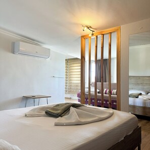 A hotel room with a bed, a small table, a sofa, a wooden partition, and a mirror.