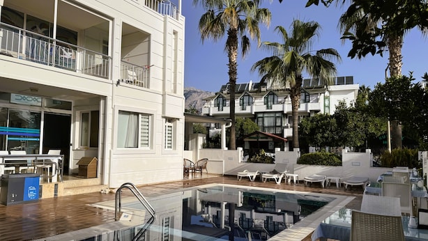 A pool area with lounge chairs, a glass-enclosed pool, and a building with balconies and a restaurant. - Amsterdam Otel & Suites  (Kemer)