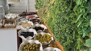 A buffet with various food items in white bowls, a white counter, and a green wall with plants. - Amsterdam Otel & Suites  (Kemer)