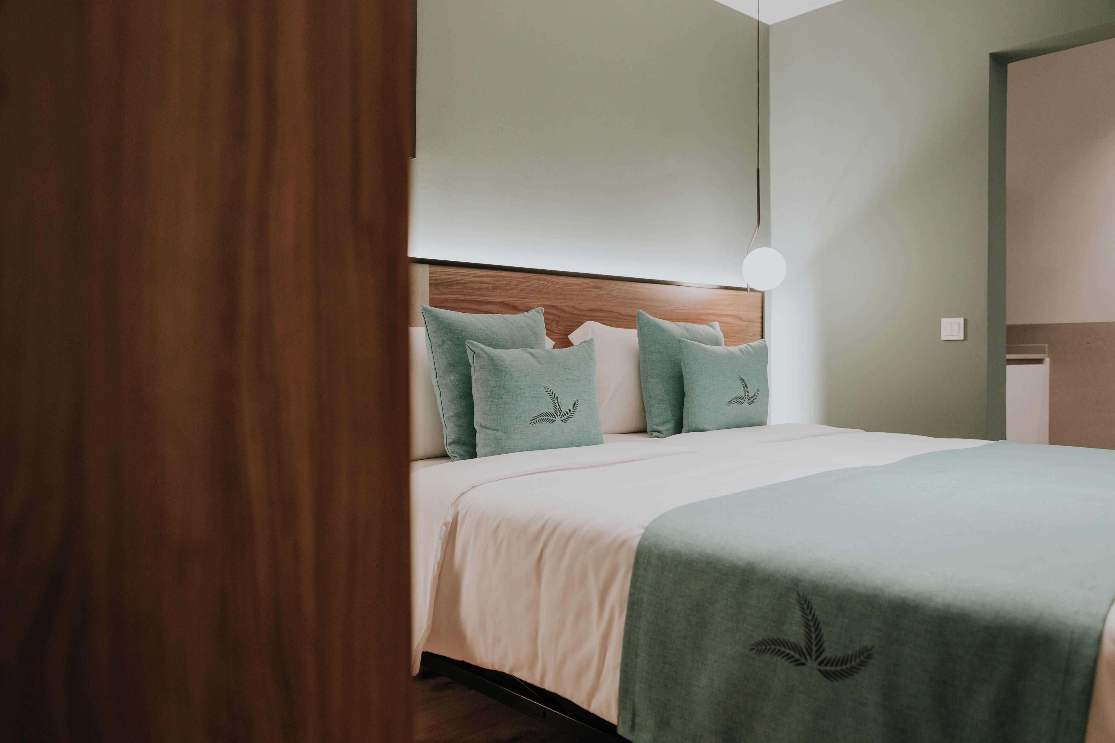 Un lit bien fait, avec une tête de lit en bois, une couverture verte et des coussins assortis.
