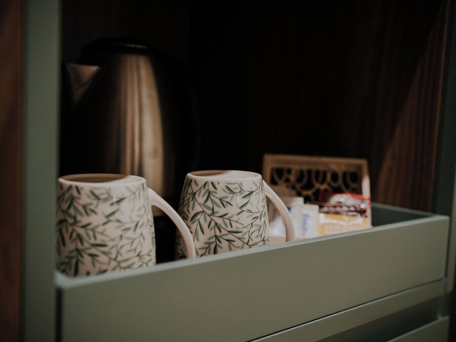 A drawer with two white mugs with a bamboo pattern, a stainless steel kettle, and a small framed picture.
