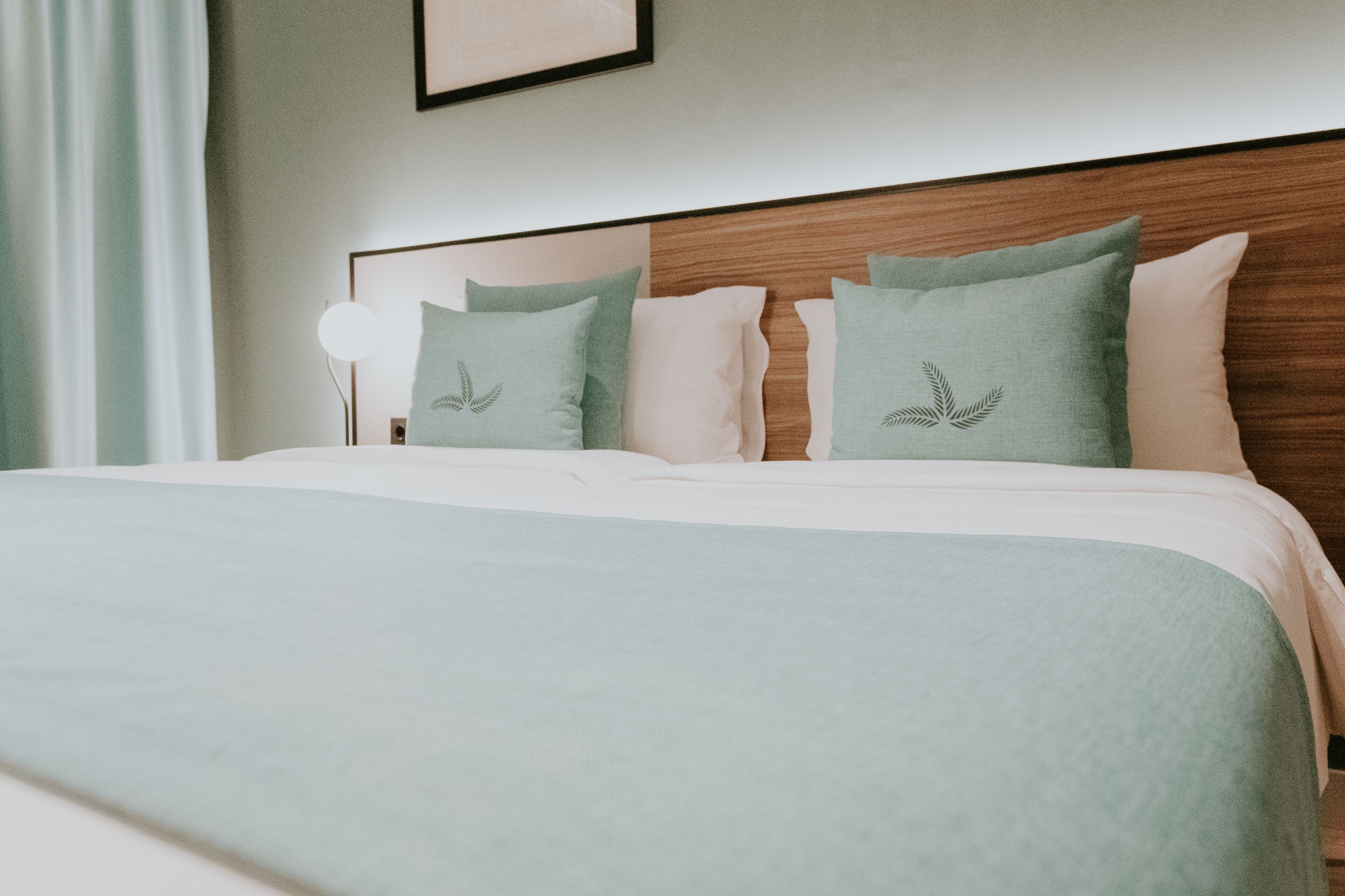 A neatly made bed with a light green bedspread and pillows, a wooden headboard, and a bedside lamp.