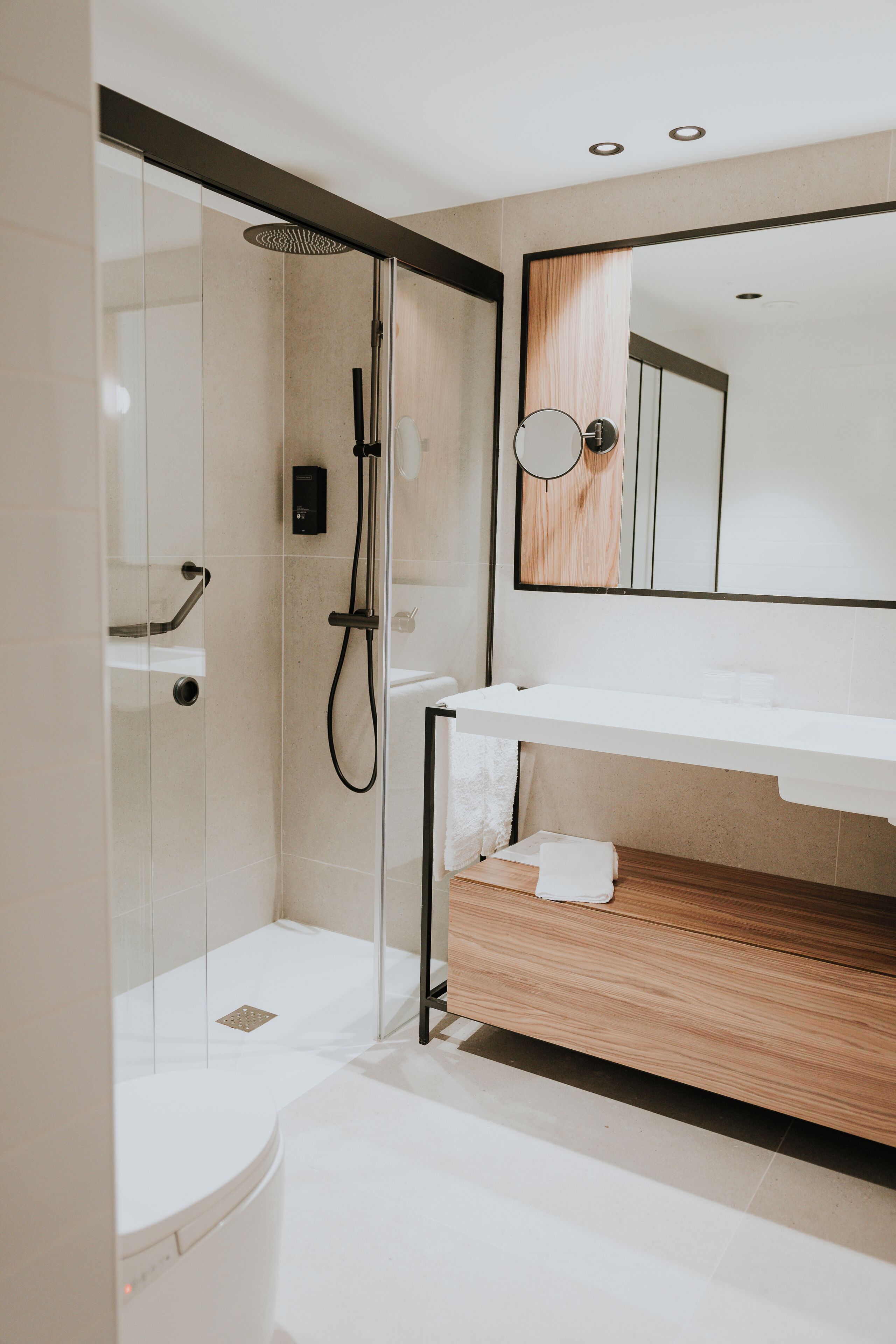 A modern bathroom with a glass-enclosed shower, a white sink, and a wooden vanity.