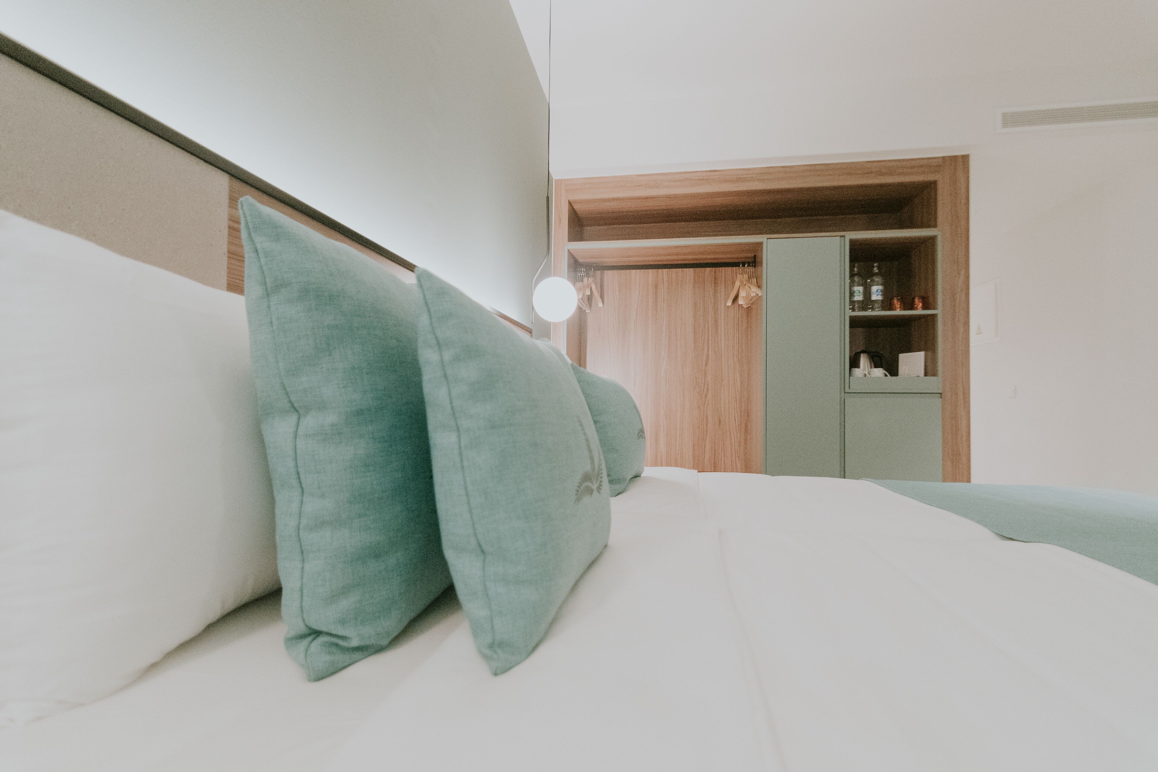 Un lit bien fait, agrémenté d’oreillers verts, une lampe de chevet et une armoire en bois avec un miroir.
