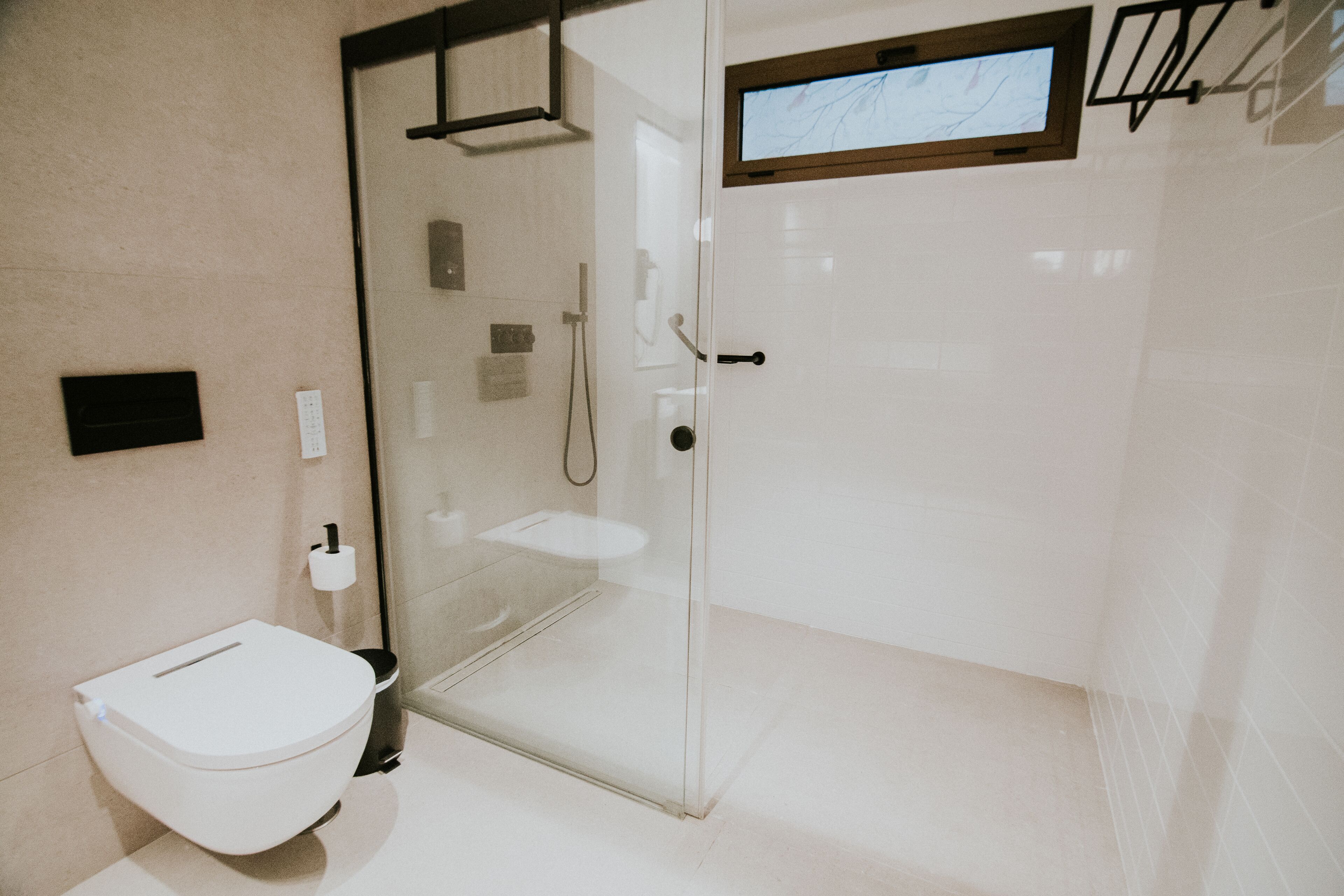 A modern bathroom with a glass shower enclosure, a toilet, and a small window above the sink.