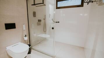 A modern bathroom with a glass shower enclosure, a toilet, and a small window above the sink.