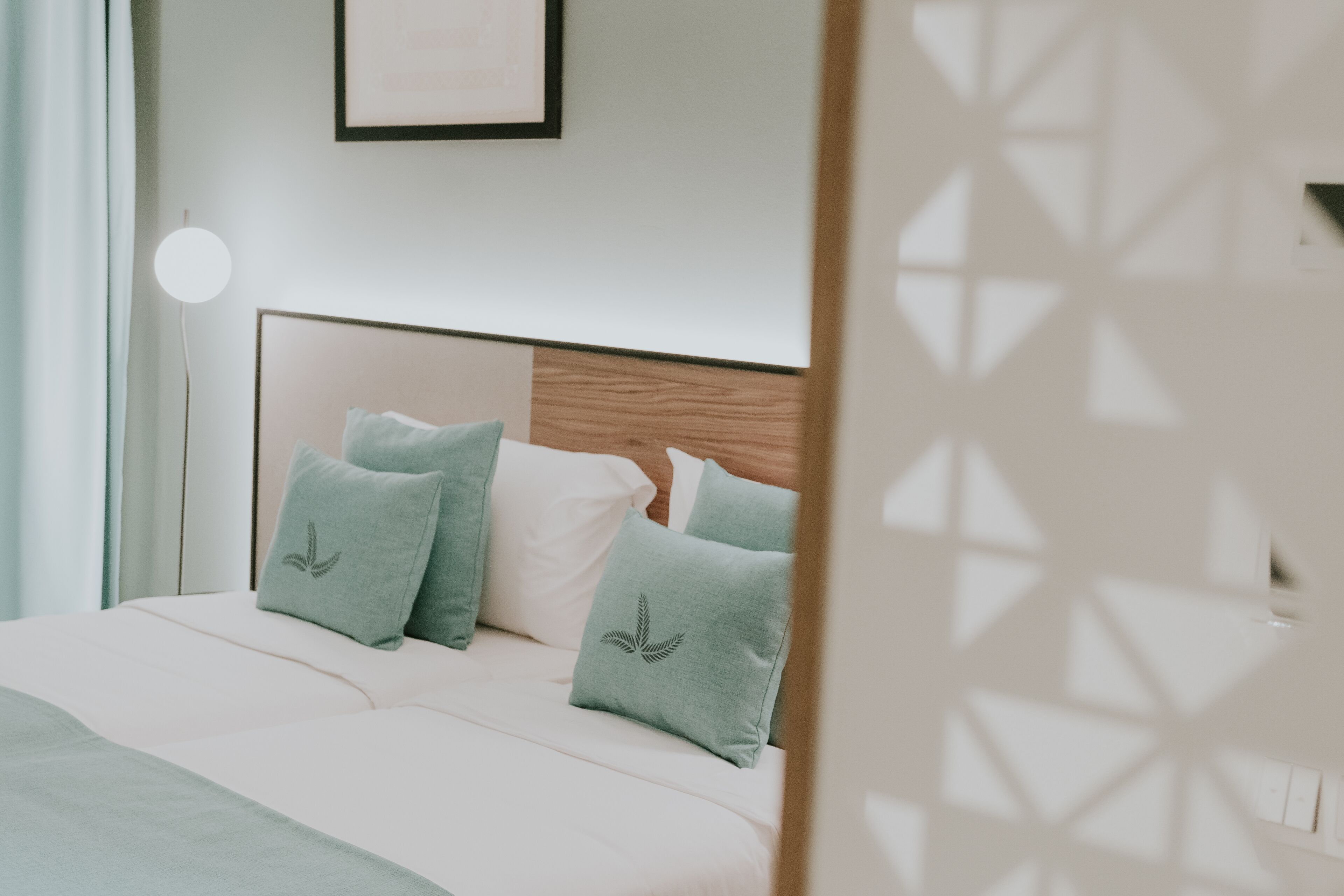 A neatly made bed with a wooden headboard, a bedside lamp, and a framed picture on the wall.