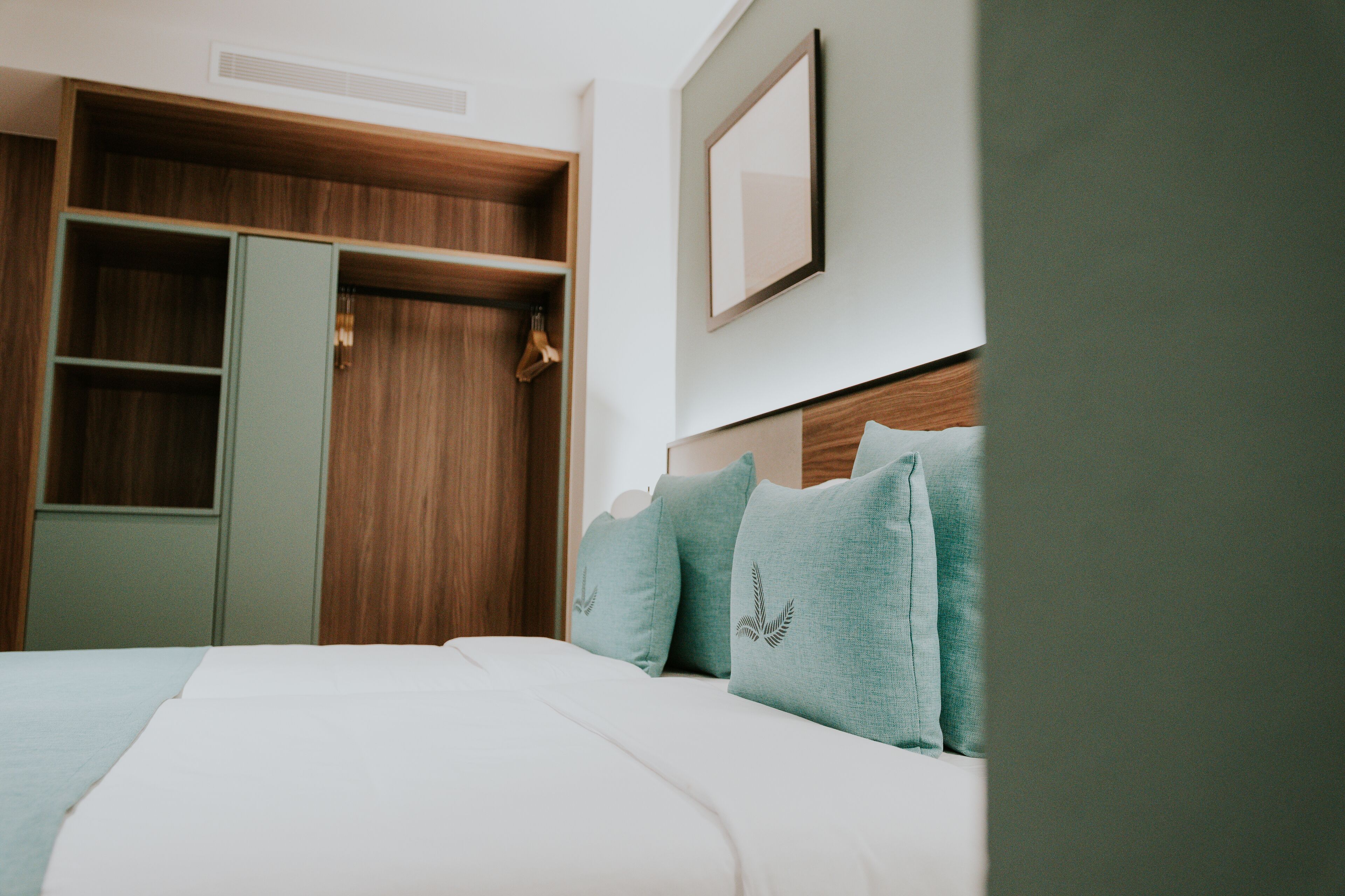 Ett hotellrum med en säng, en garderob och en inramad tavla på väggen.