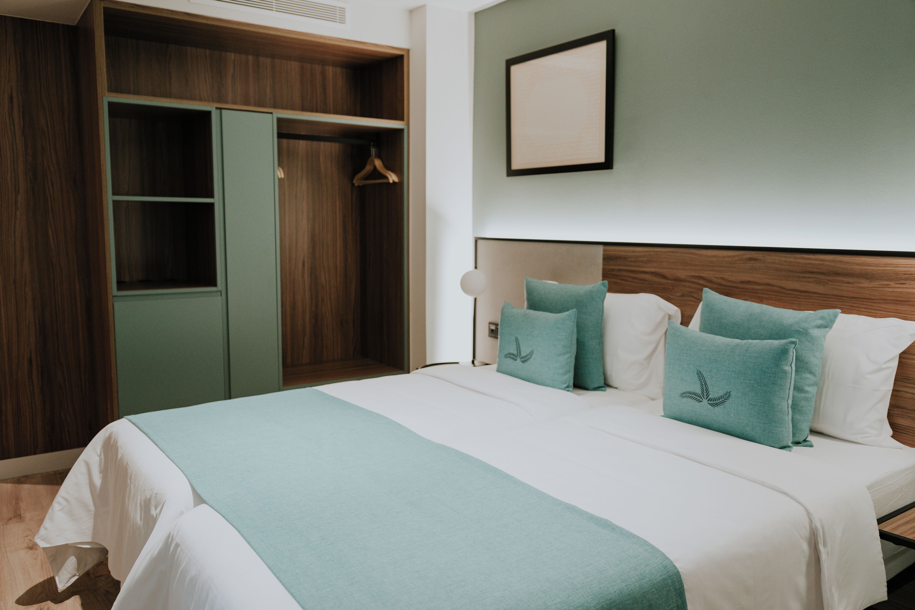 A hotel room with a bed, a wardrobe, and a framed picture on the wall.