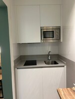 Una cocina compacta con alacenas blancas, un lavamanos de acero inoxidable y un microondas.