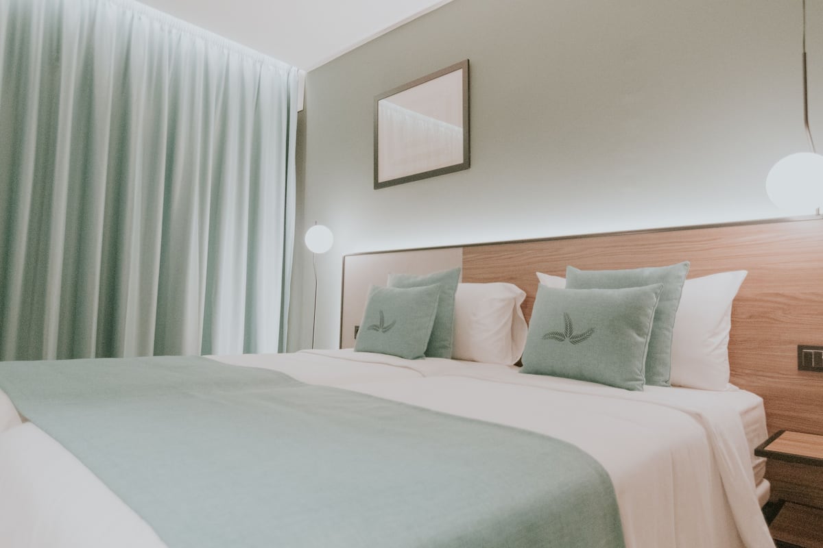 Une chambre d’hôtel avec un lit, une table de chevet, une lampe et une fenêtre avec des rideaux.