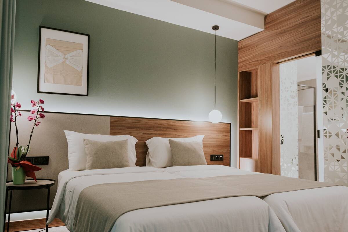 Une chambre d’hôtel moderne avec un grand lit, une table de chevet ornée d’un vase de fleurs, un tableau encadré au mur et une tête de lit en bois.