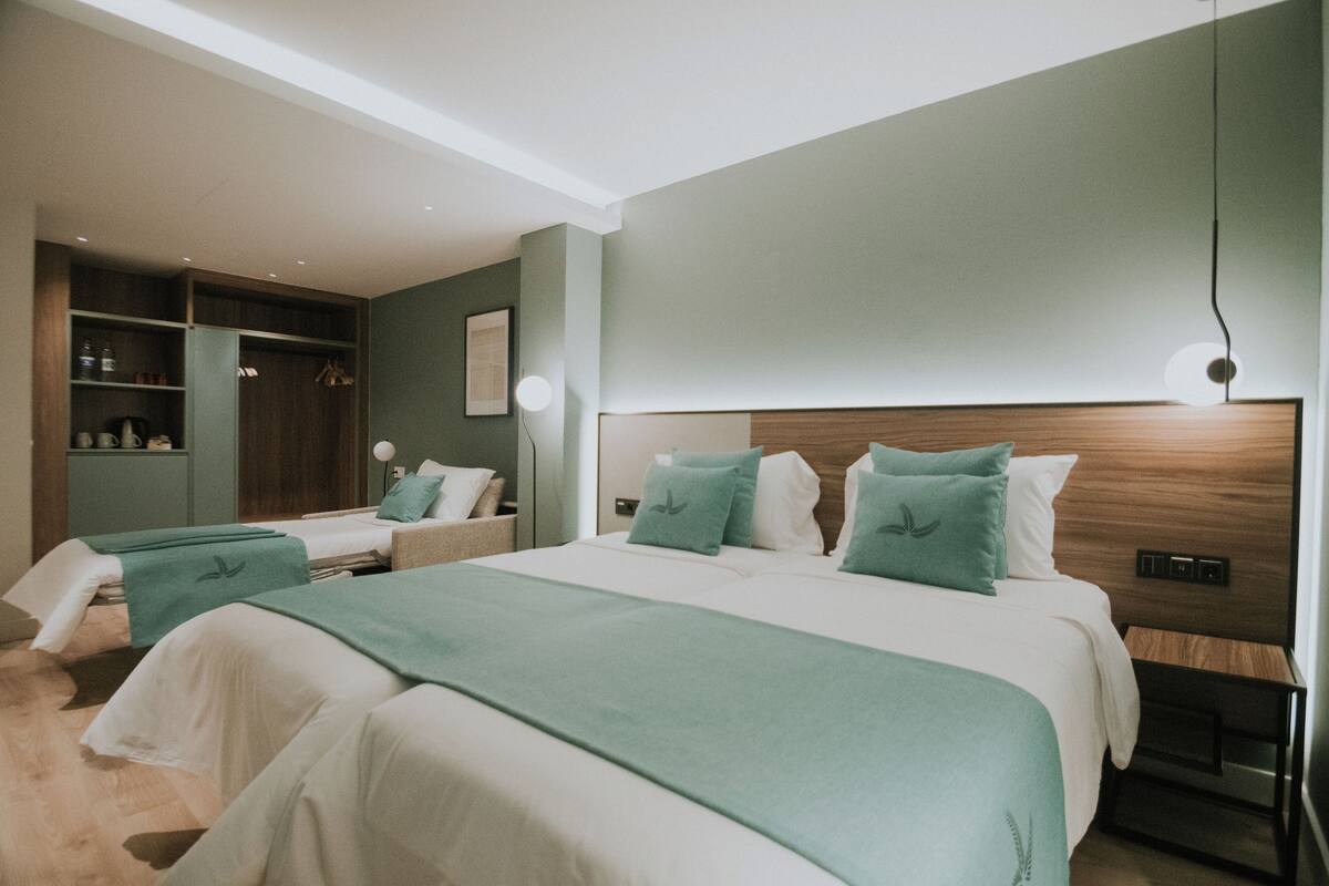 Une chambre d’hôtel moderne avec deux lits, une armoire intégrée et une table de chevet avec une lampe.