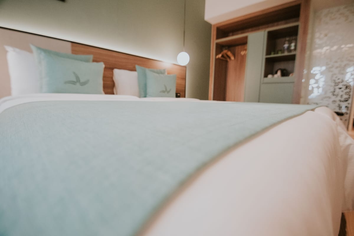 Un lit bien fait, avec une couvre-lit bleu clair et des oreillers, une tête de lit en bois et une table de chevet avec une lampe.