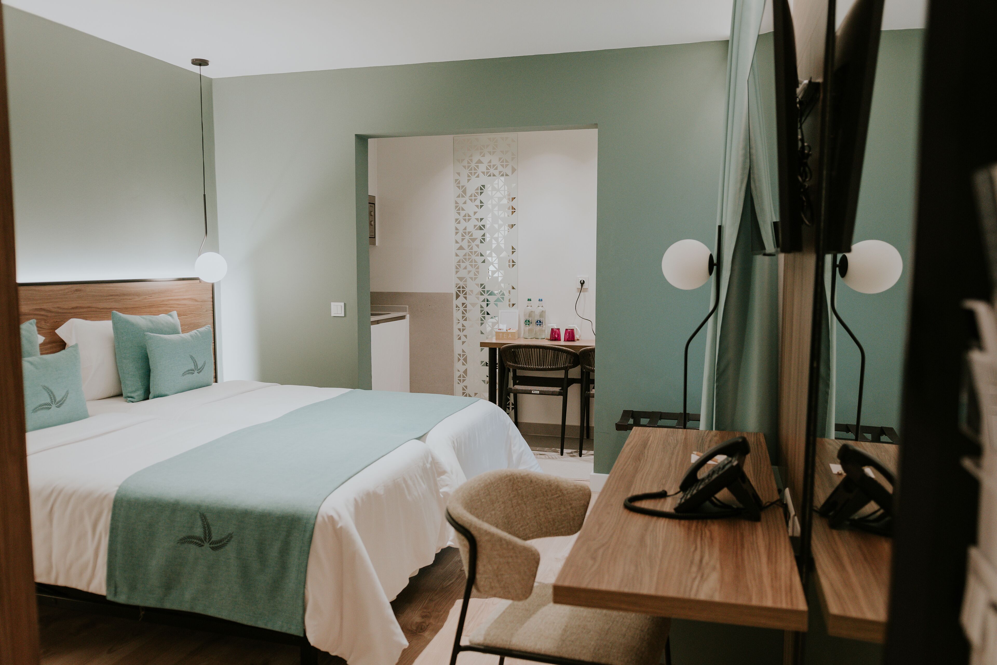 A hotel room with a bed, a desk, a chair, a telephone, and a mirror.