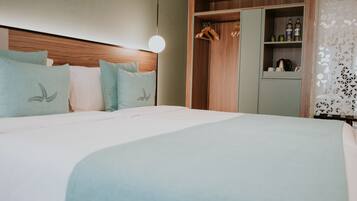 Une chambre d’hôtel avec un grand lit, une tête de lit en bois, une armoire où sont suspendus des vêtements et une étagère avec des bouteilles.