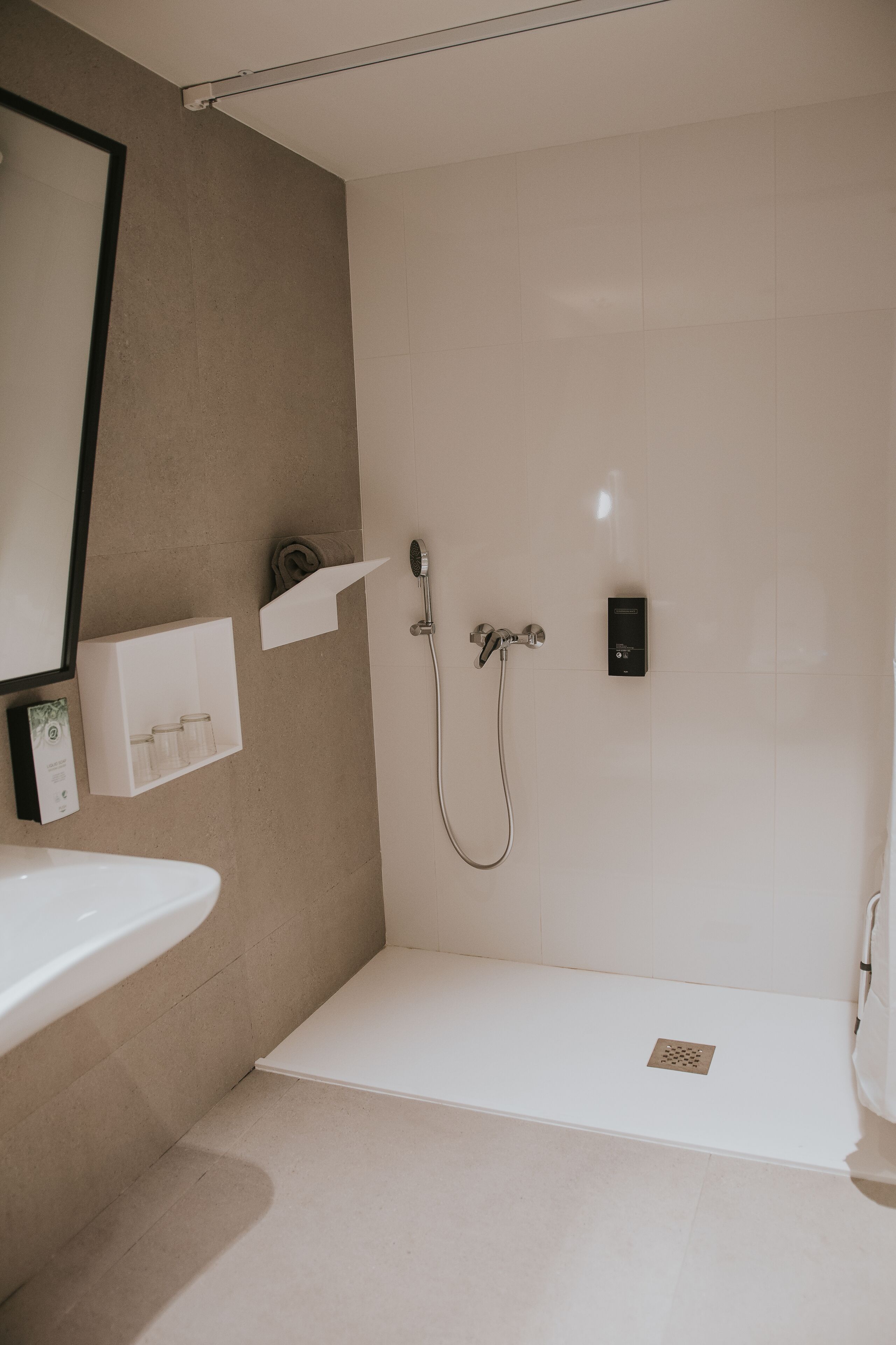Un baño moderno con un lavamanos blanco, una ducha con cabezal de ducha manual y un perchero.