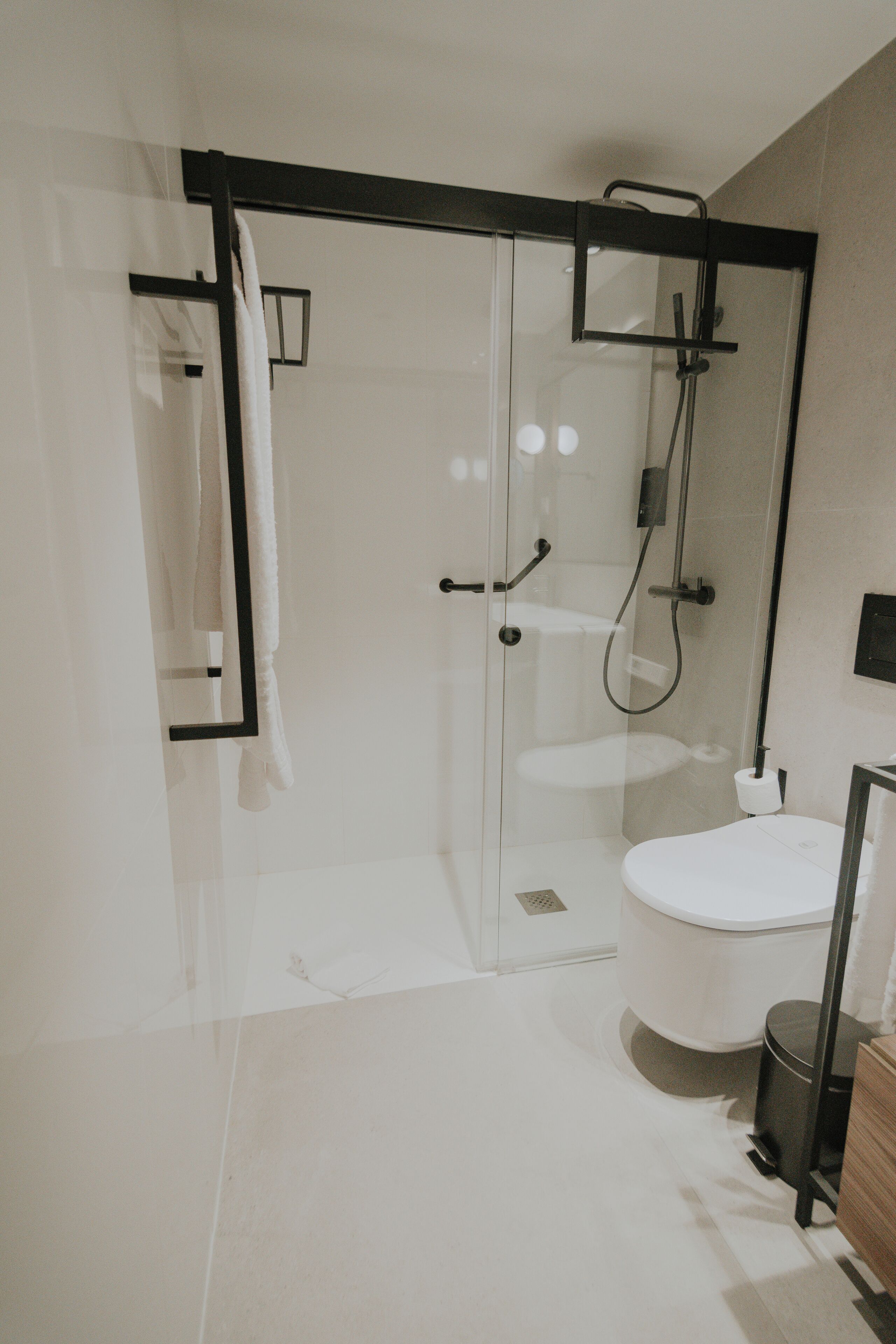 Une salle de bain moderne avec une douche à parois de verre, des toilettes blanches et une poubelle noire.