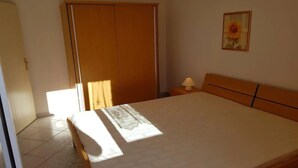 Quarto com cama grande, guarda-roupa, mesa de cabeceira com abajur e um quadro na parede.