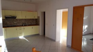Uma cozinha espaçosa com armários amarelo claro, piso revestido e uma porta que dá para outro cômodo.