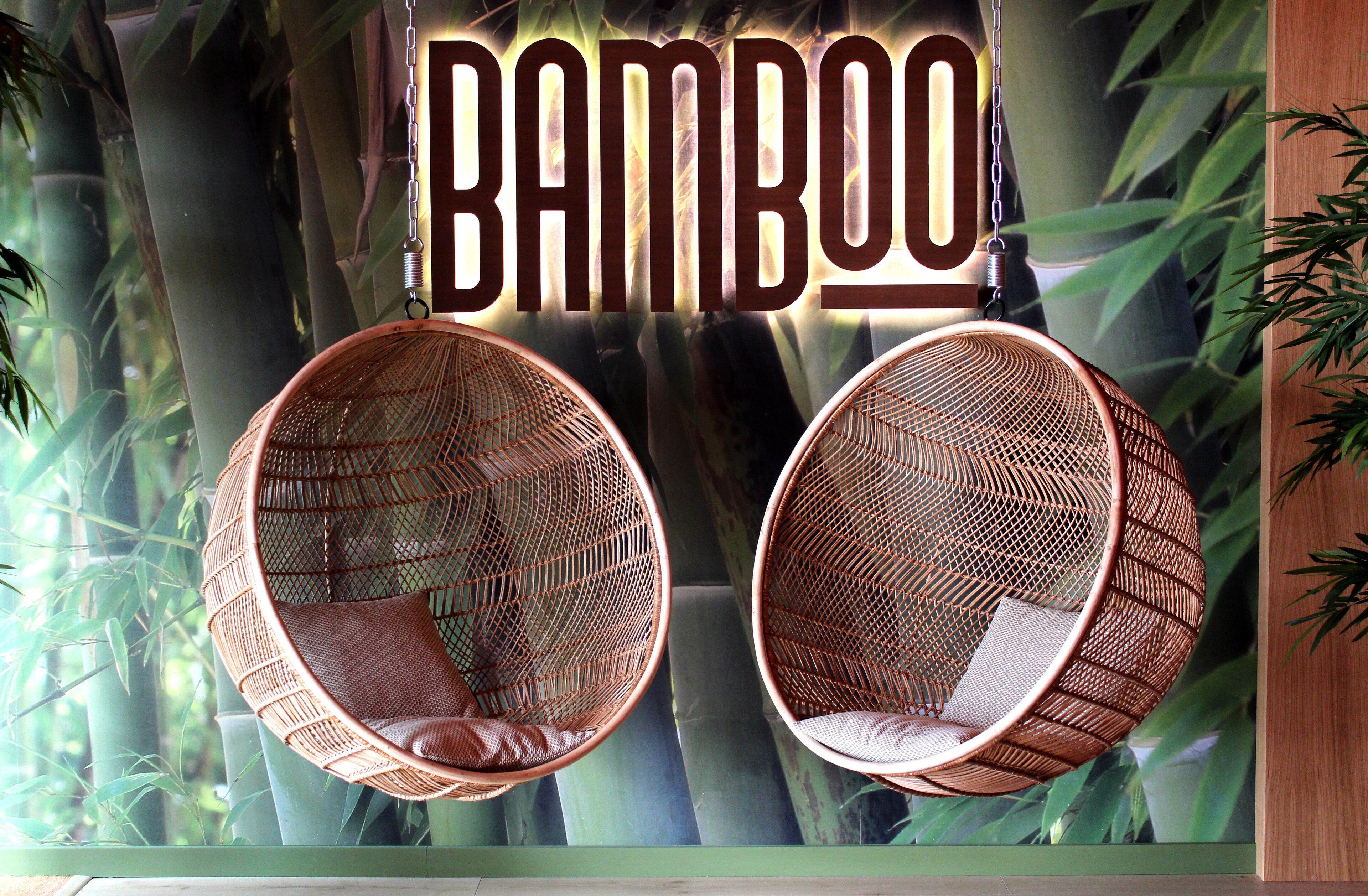 Dos sillones colgantes de mimbre con cojines, suspendidos del techo donde se ilumina la palabra 'Bamboo'.