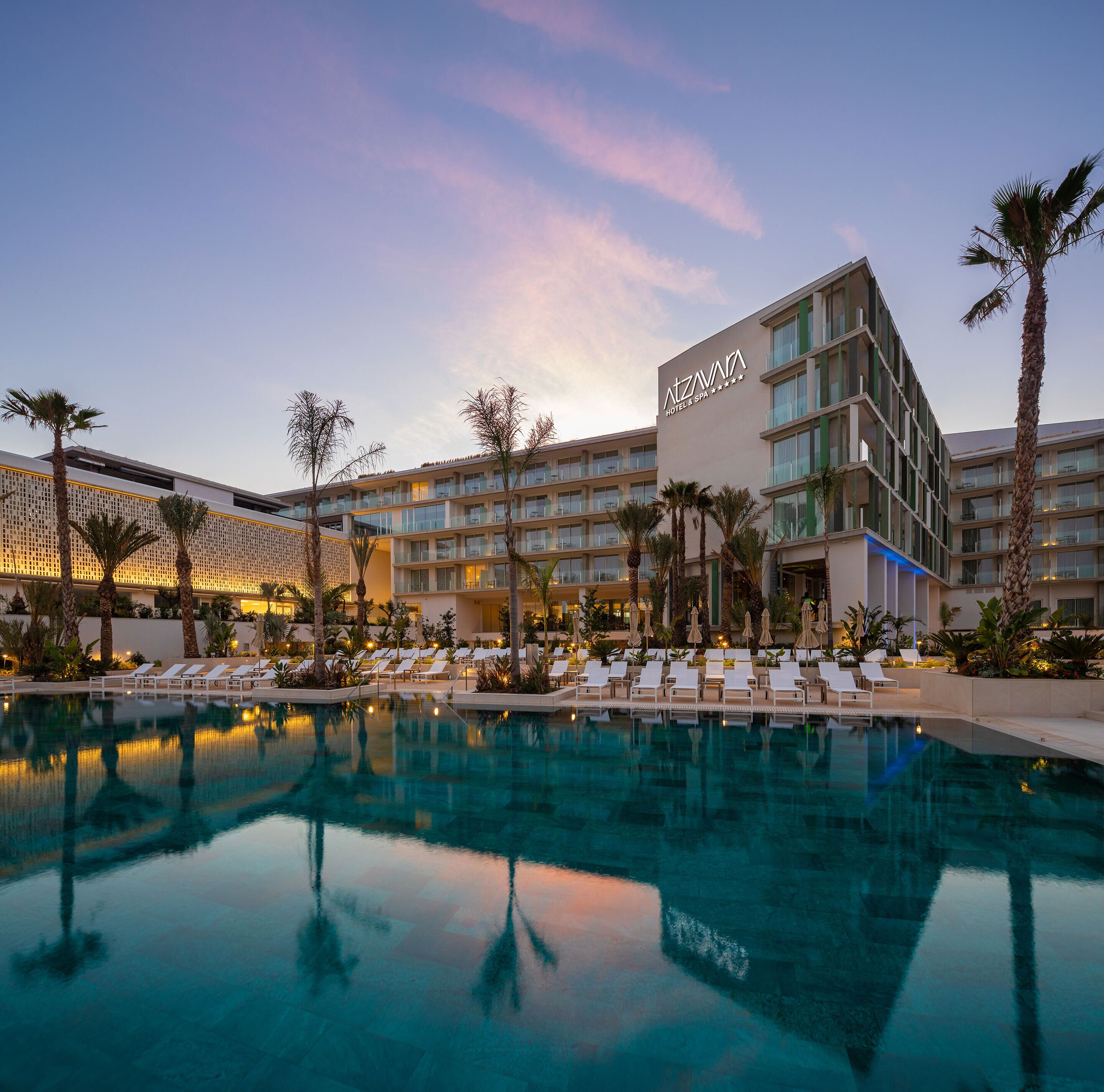 Un hotel amb piscina, palmeres i una façana d'edifici moderna.