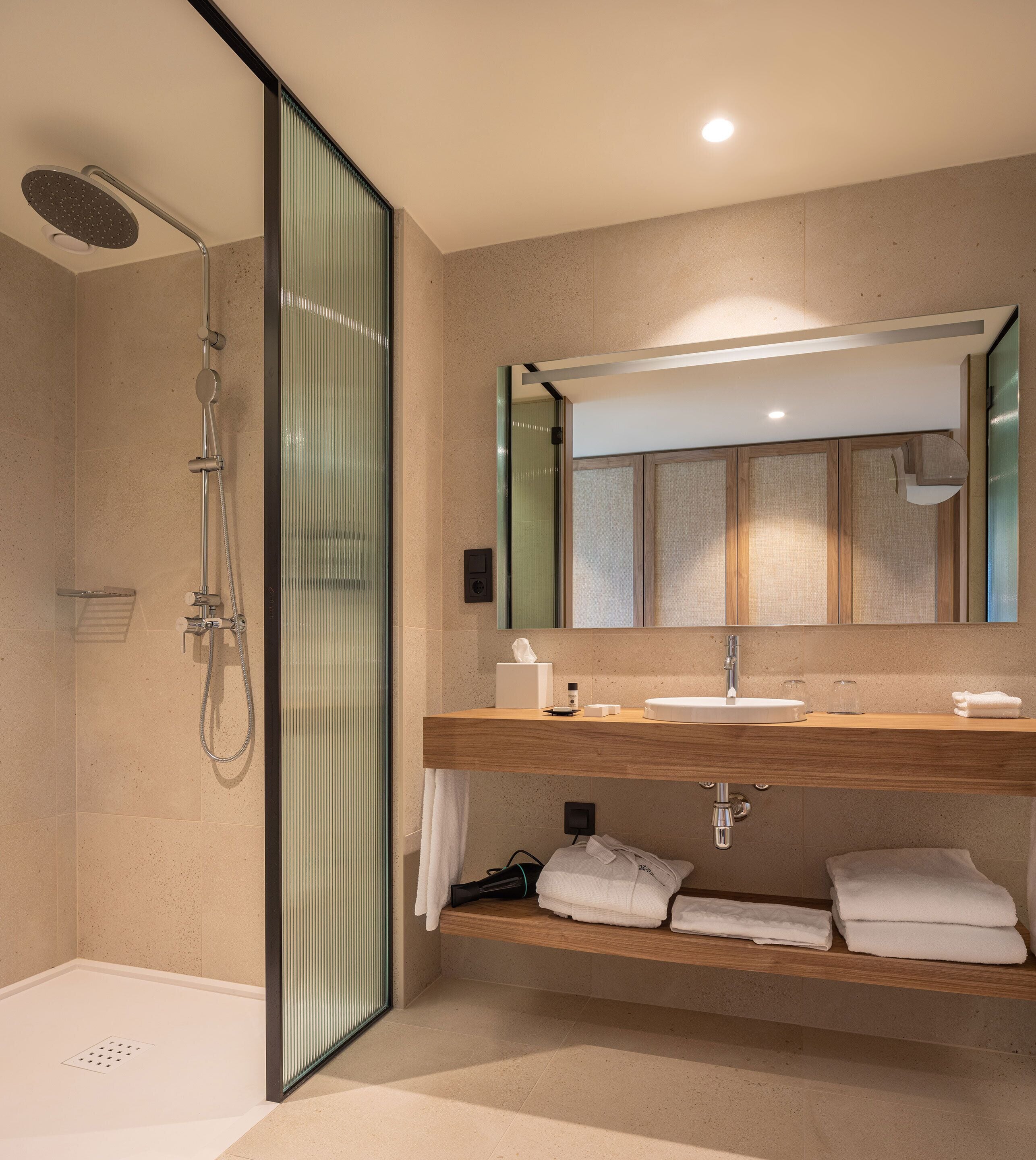 Un baño moderno con cabina de ducha de vidrio, tocador de madera y un espejo grande.