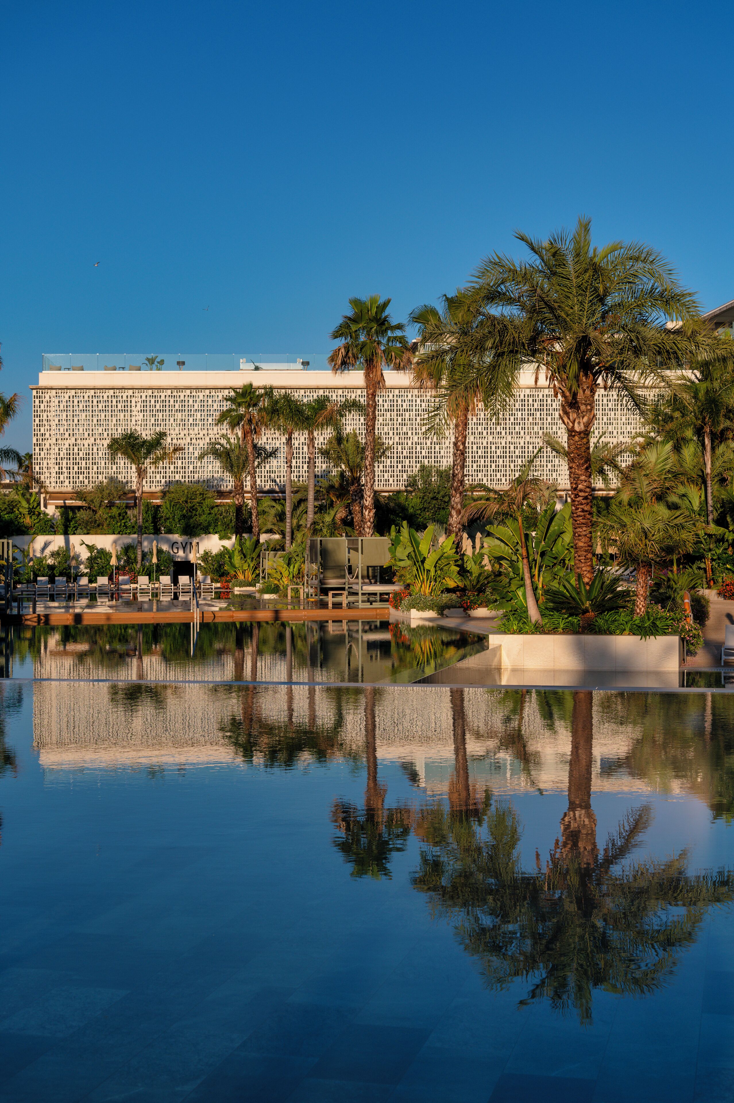 A large hotel with a reflective pool, palm trees, and a modern architectural design.