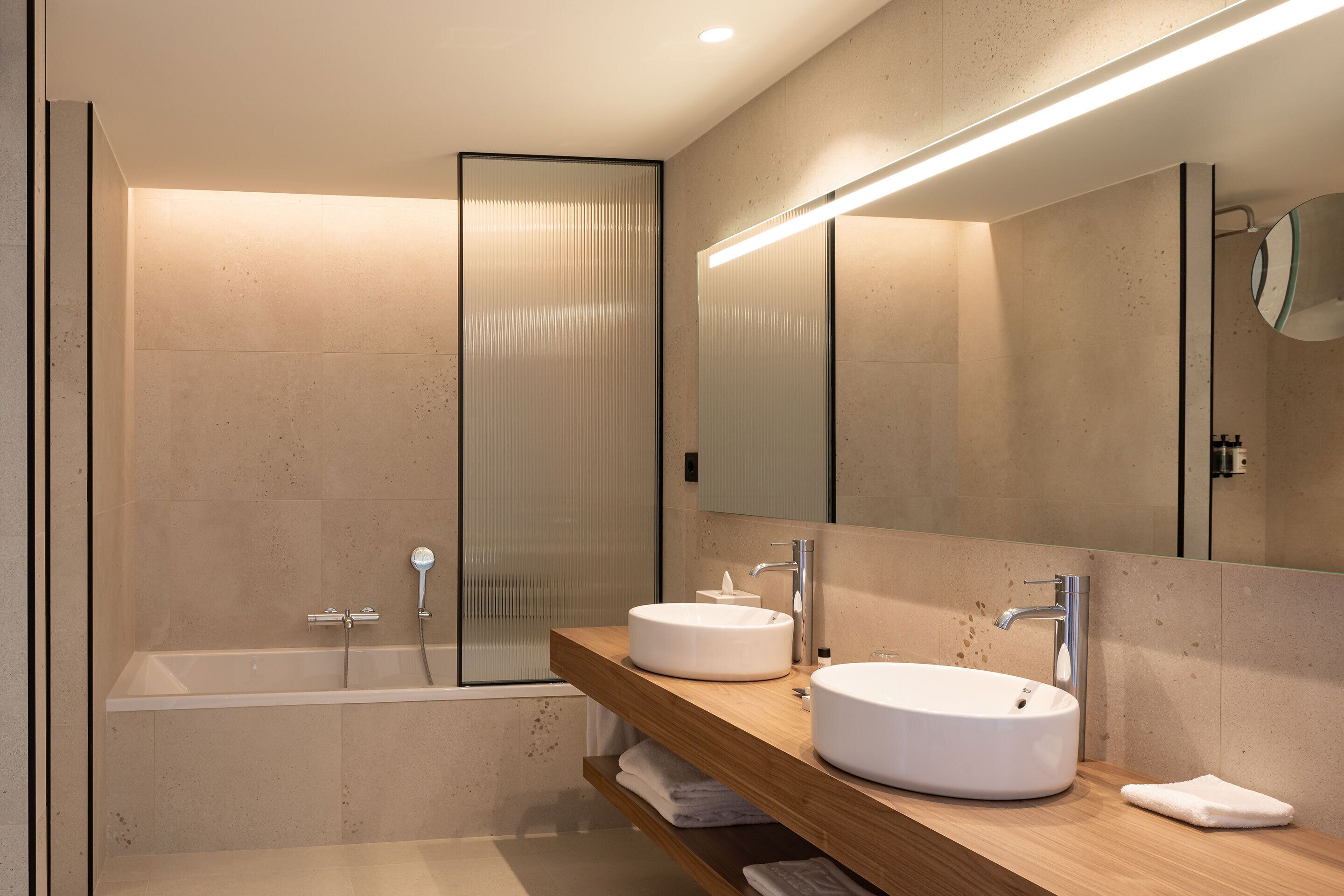 A modern bathroom with a bathtub, two sinks, a large mirror, and a towel rack.