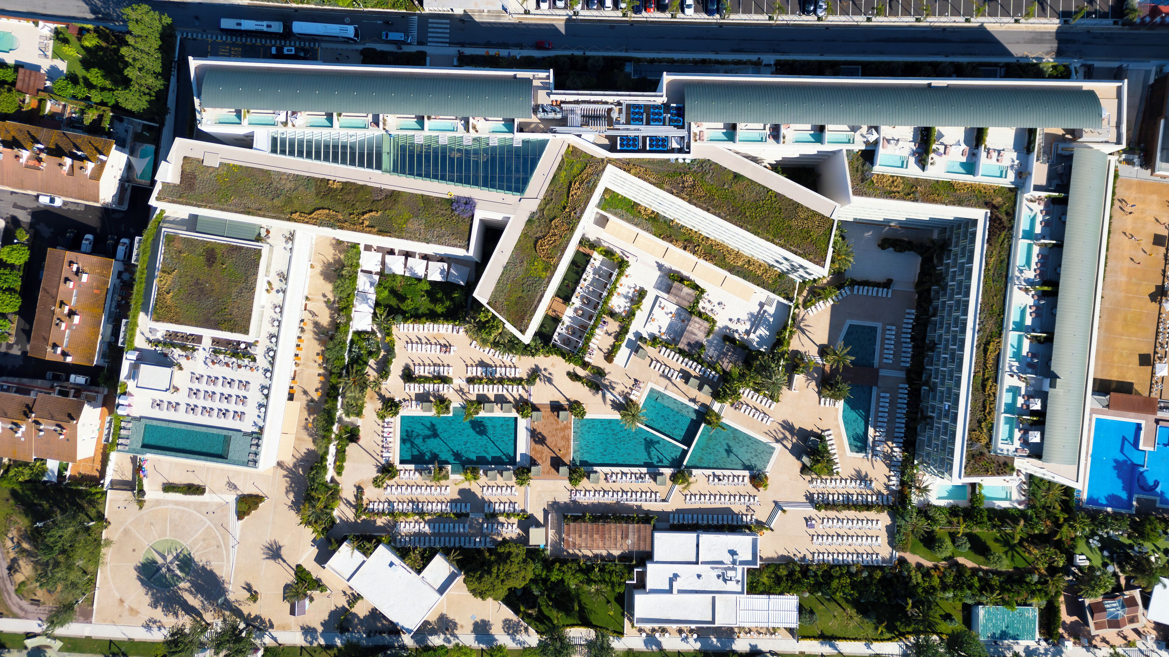An aerial view of a hotel with multiple swimming pools, sun loungers, and a rooftop area.