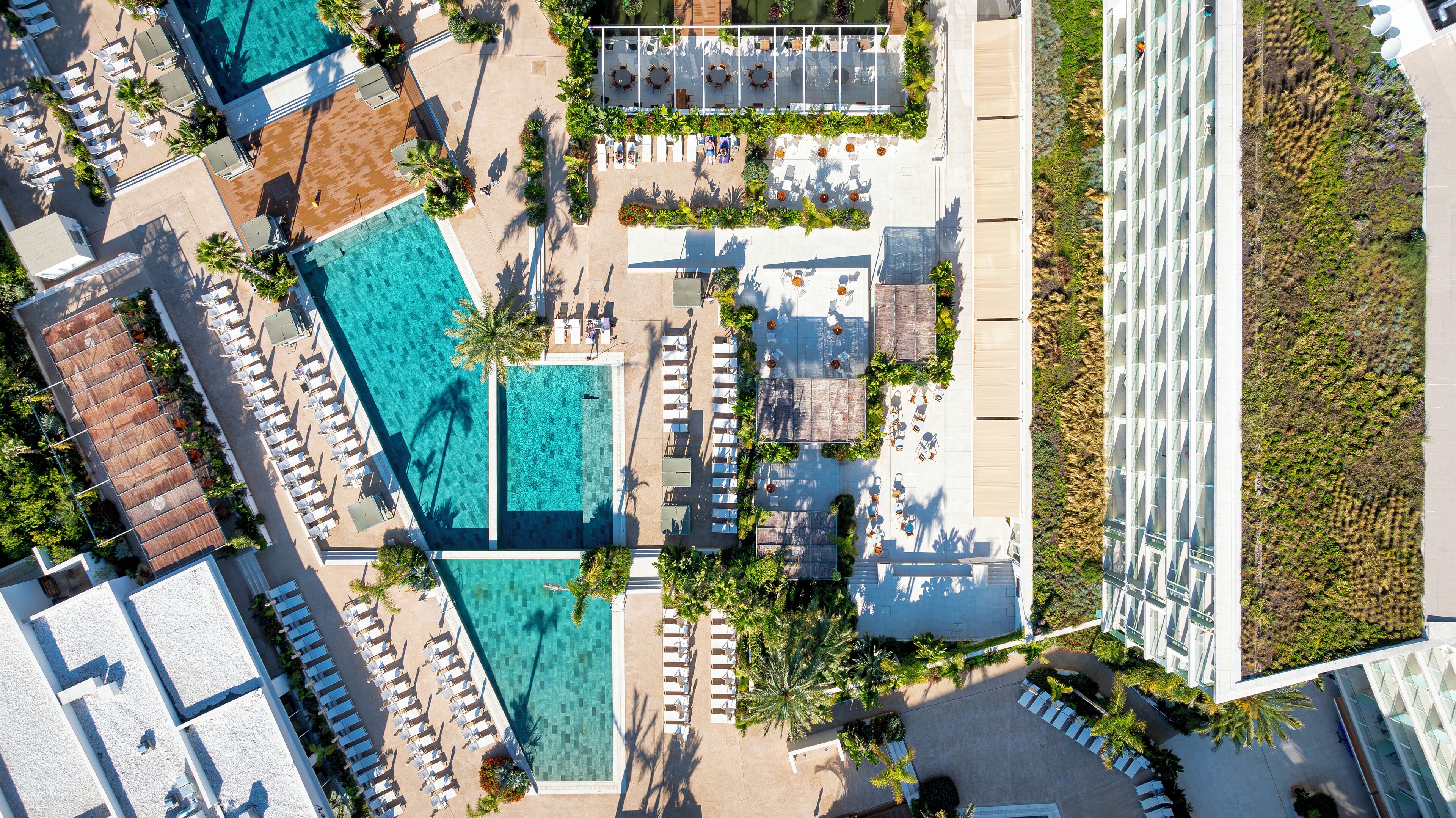 Vista aérea de un complejo turístico con varias piscinas, tumbonas y un jardín en la azotea.