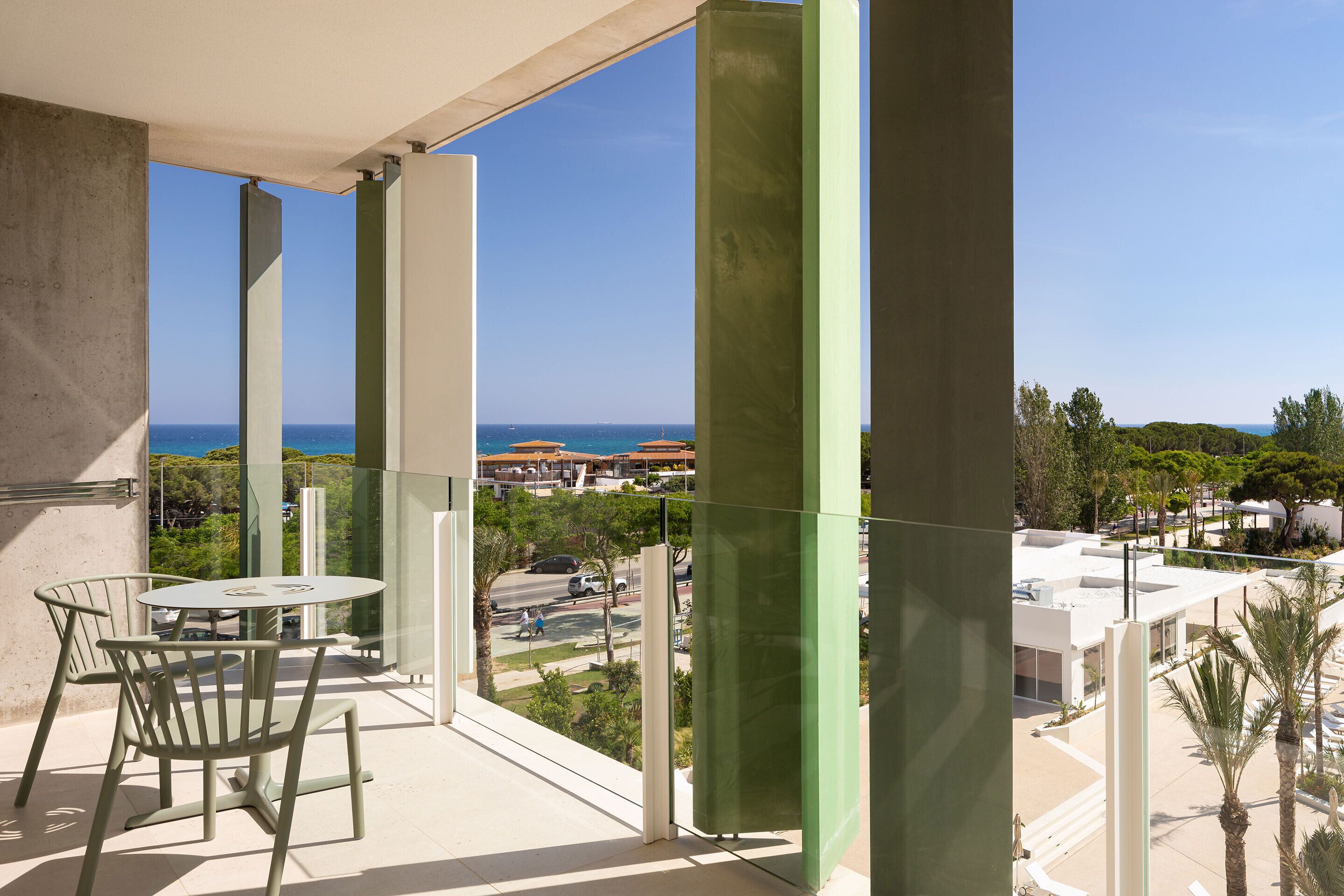 Un balcón con mesa y sillas, con vistas al mar y edificios, con zonas verdes.