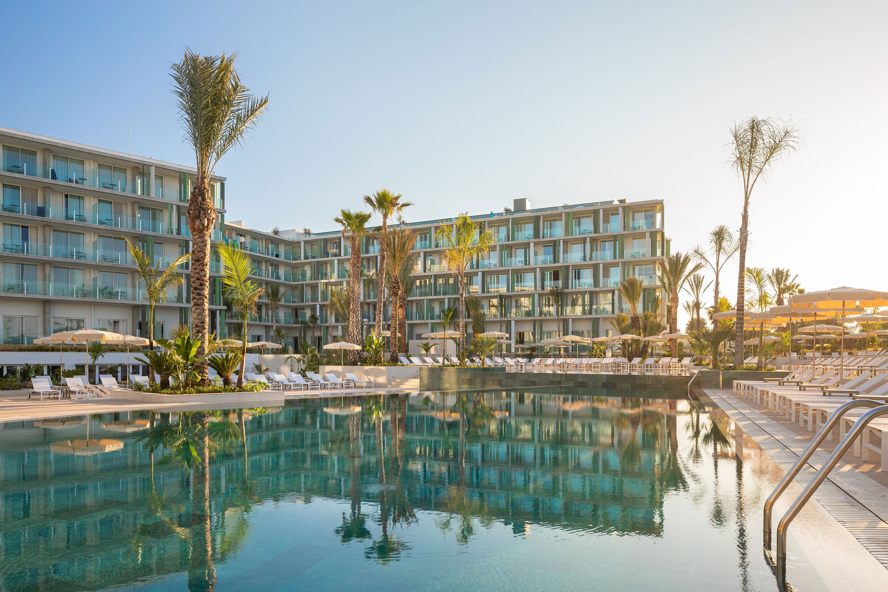 Un hotel con piscina, palmeras y tumbonas.
