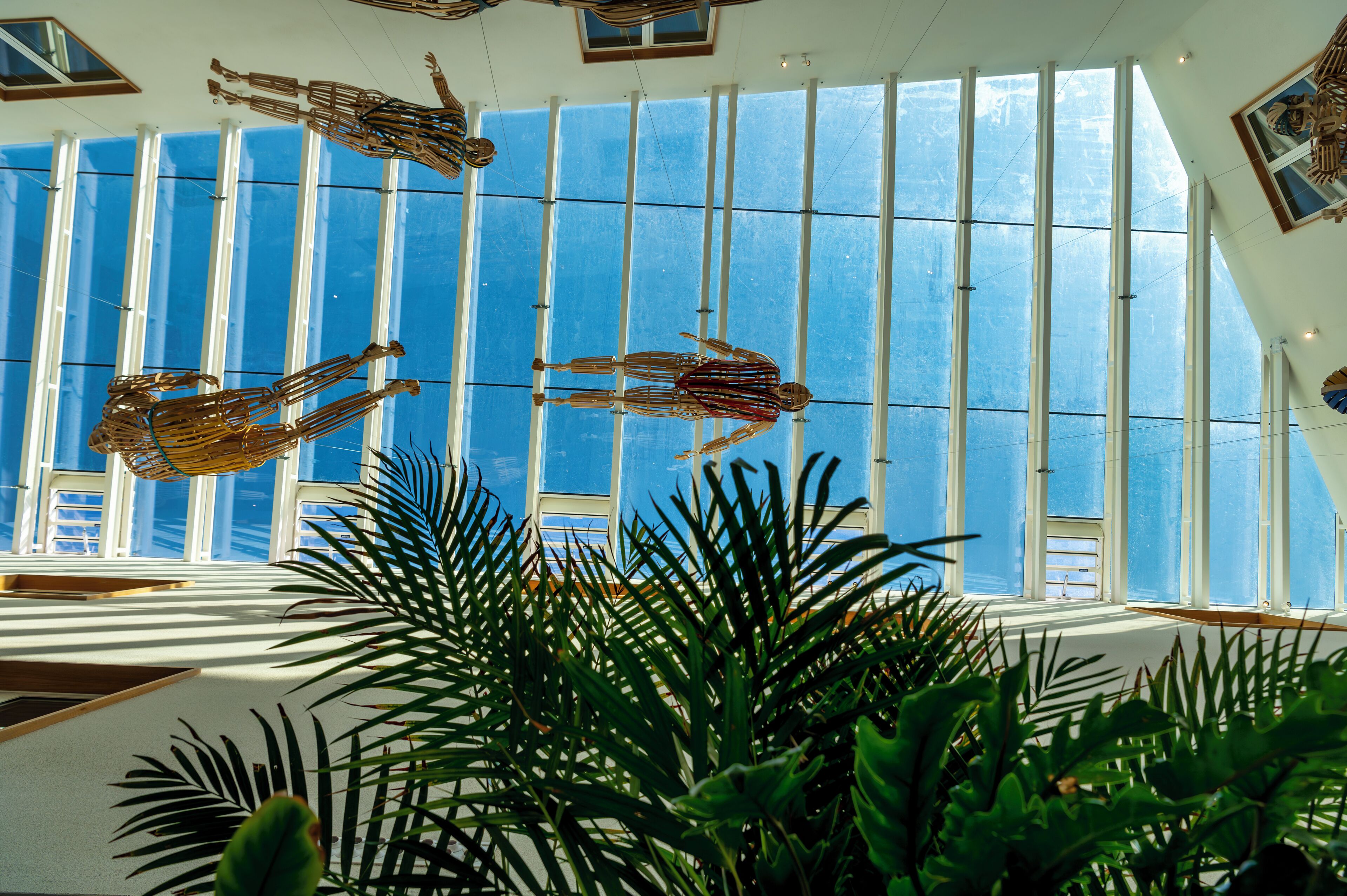 A room with large windows, a ceiling sculpture, and indoor plants.