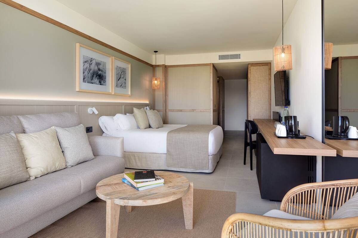 Ein modernes Hotelzimmer mit einer Couch, einem Bett, einem Esstisch und einem kleinen runden Tisch mit Büchern.