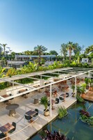 Un patio al aire libre con mesas y sillas, rodeado de abundante vegetación y un pequeño elemento acuático.