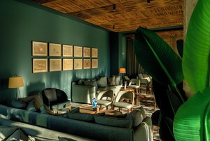 Una sala de estar moderna con un sofá, sillones y una mesa de centro. Hay cuadros enmarcados en la pared y una planta grande en la esquina.