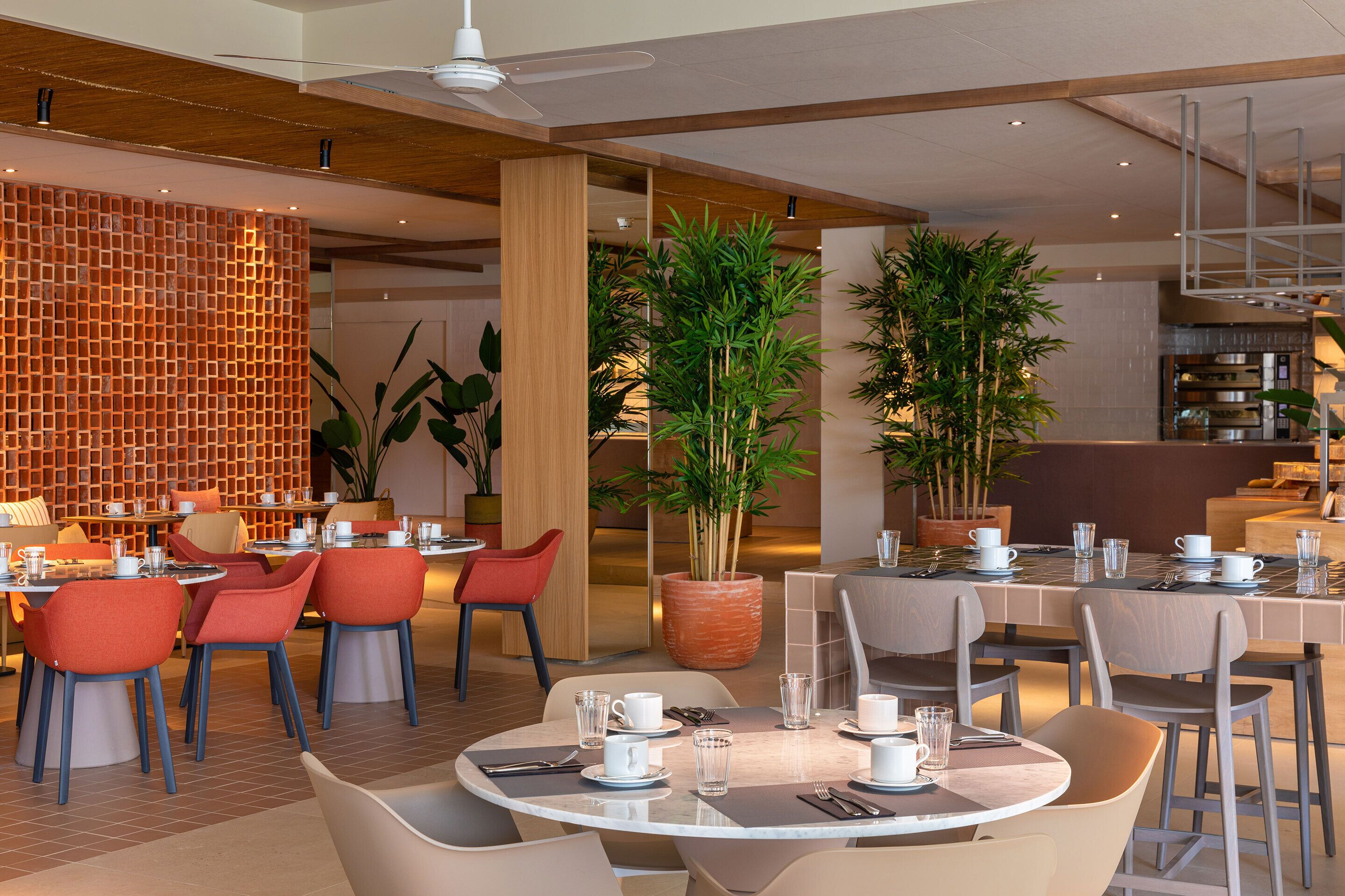 A modern dining area with round tables, red and grey chairs, and potted plants.