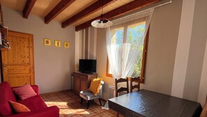 A cozy living room with a red sofa, a dining table, and a television on a wooden cabinet. - Independent cottage - private terrace - shared swimming pool (Simeyrols)