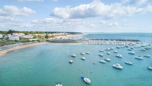 Un port de plaisance situé sur la côte, où de nombreux bateaux sont amarrés, une plage de sable et, au loin, des immeubles résidentiels.